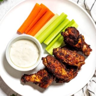 A plate of baked wings, celery, carrots, and a ramekin of ranch dressing.