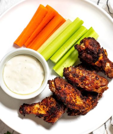 A plate of baked wings, celery, carrots, and a ramekin of ranch dressing.