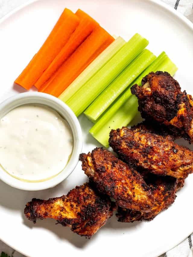 A plate of baked wings, celery, carrots, and a ramekin of ranch dressing.