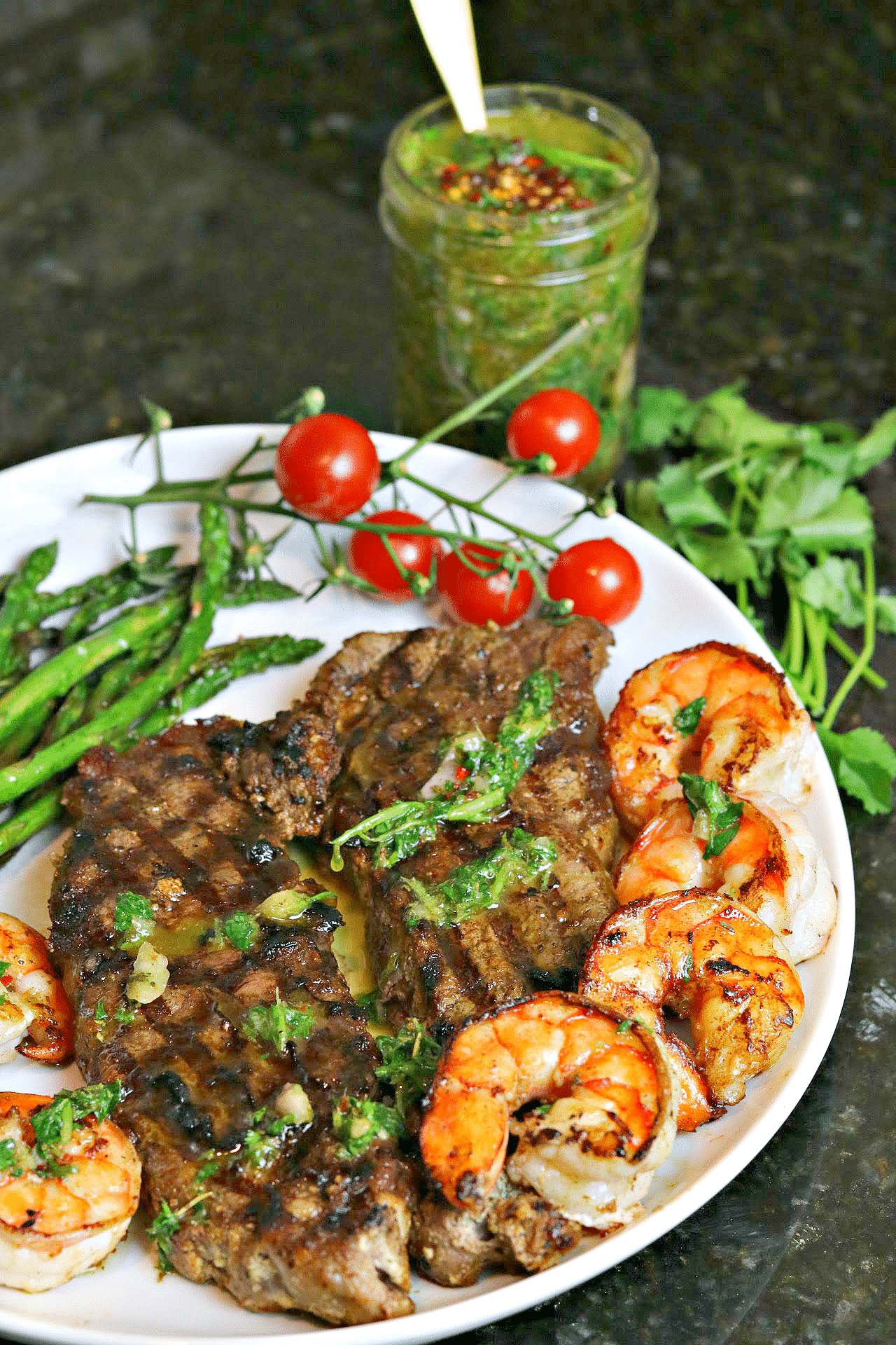 NY Strip Steak on a plate with asparagus, shrimp, and chimichurri