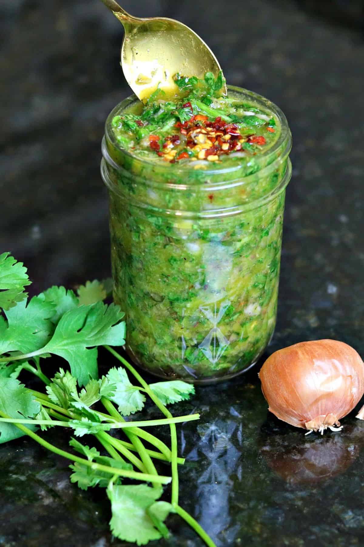 chimichurri sauce in a glass jar with parsley and a shallot