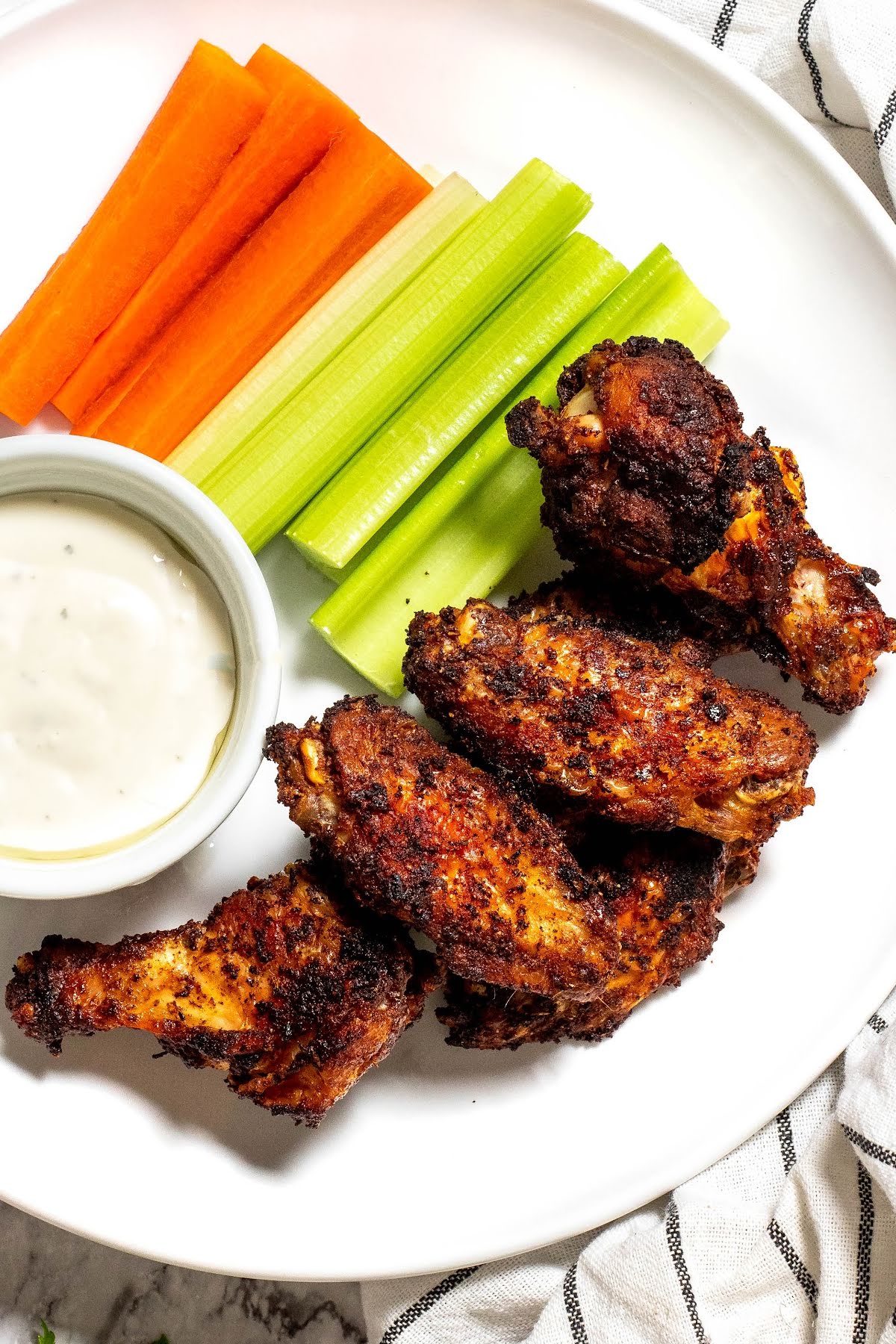 Ninja Foodi spicy dry rub chicken wings on a plate with celery, carrots, and ranch dressing 