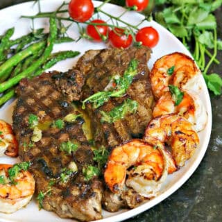 new york strip steak cooked on a plate with seared shrimp, asparagus and chimichurri