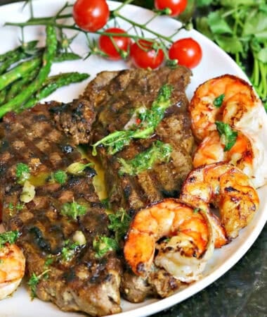 new york strip steak cooked on a plate with seared shrimp, asparagus and chimichurri