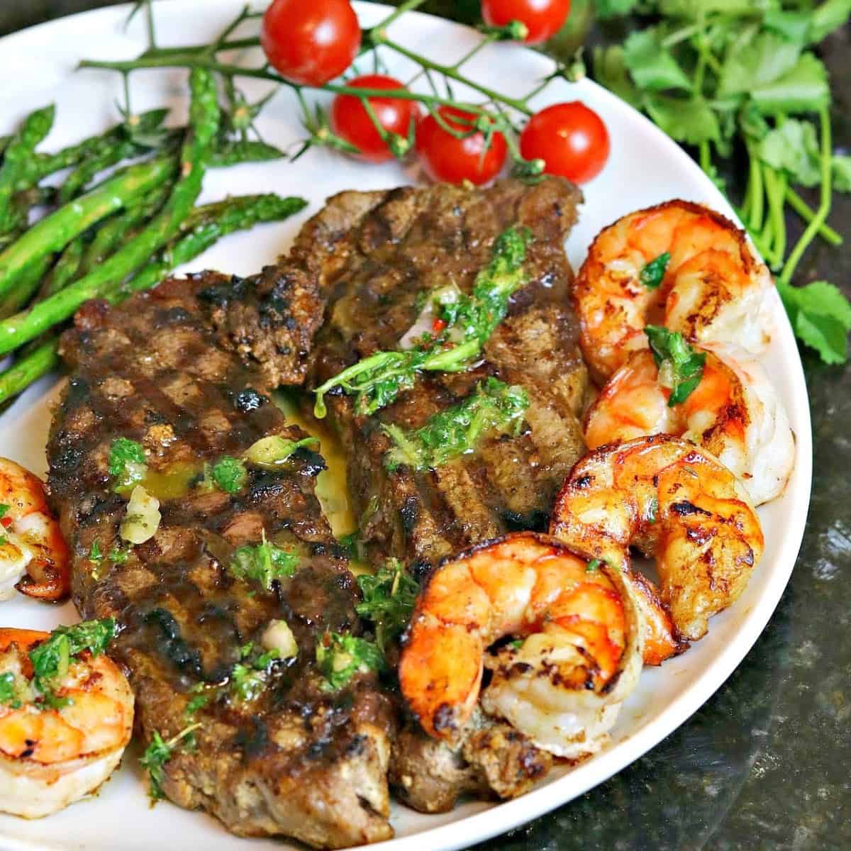 new york strip steak cooked on a plate with seared shrimp, asparagus and chimichurri