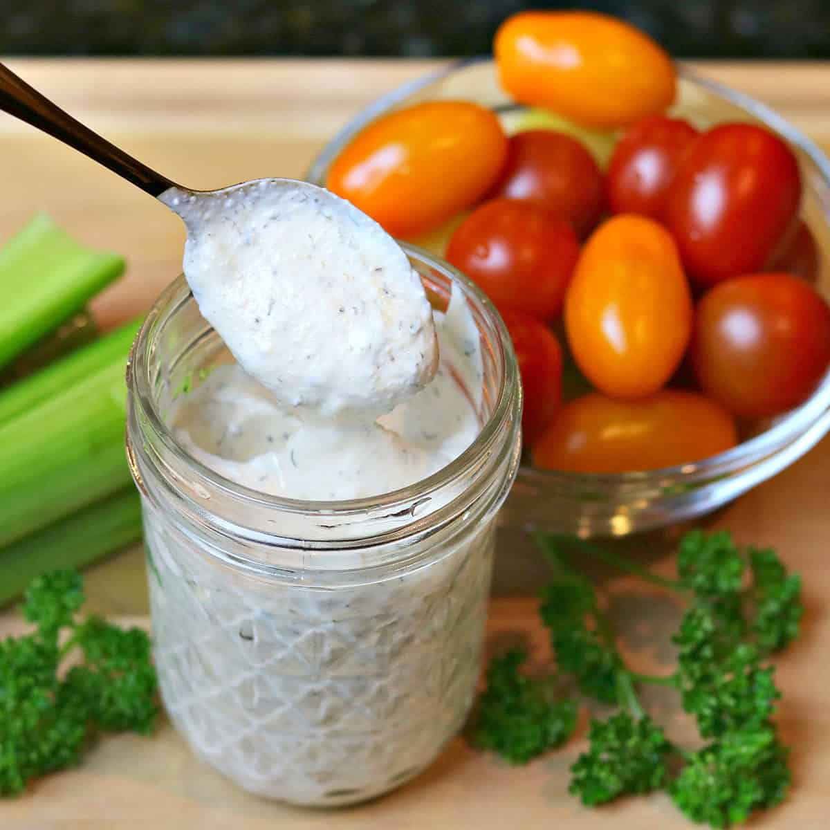 ranch dressing in a glass jar with parlsey, celery. and cherry tomatoes in separate bowls