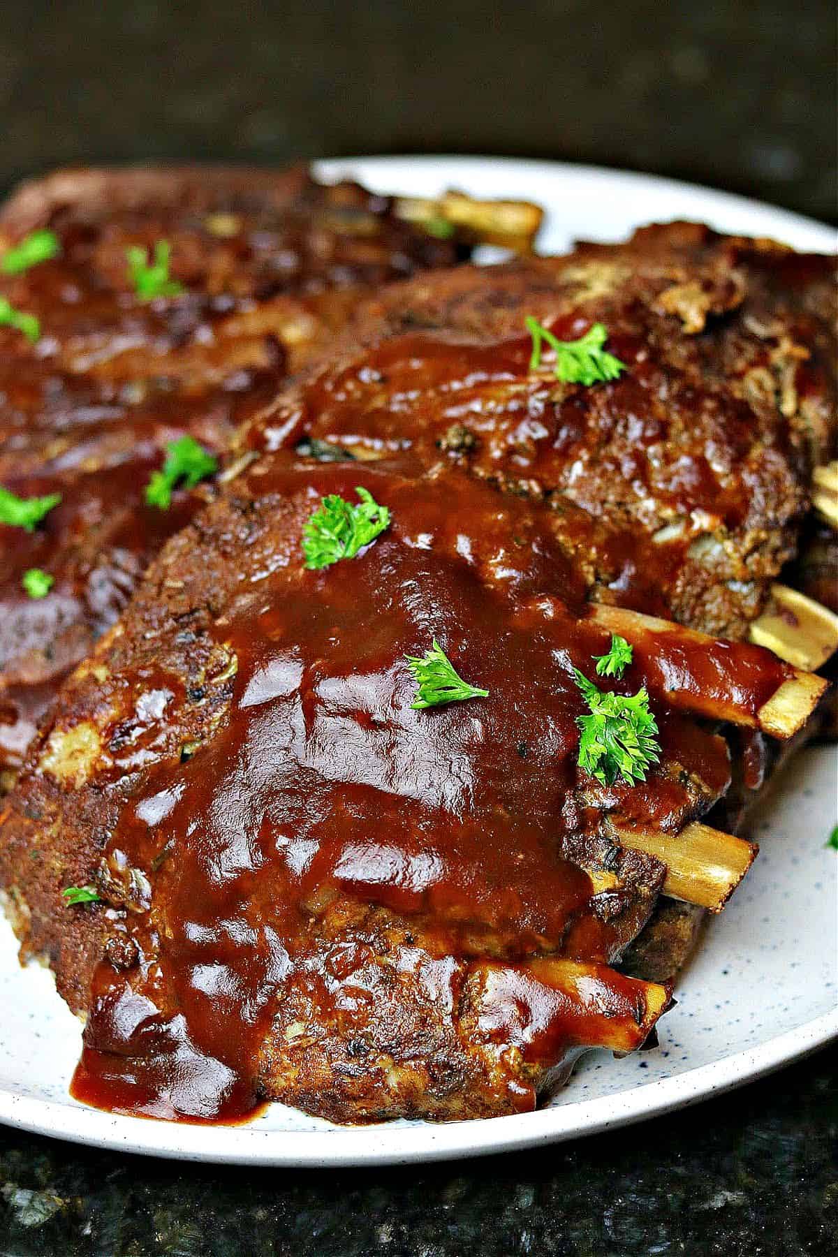 two racks of keto ribs on a plate with bbq sauce and parsley