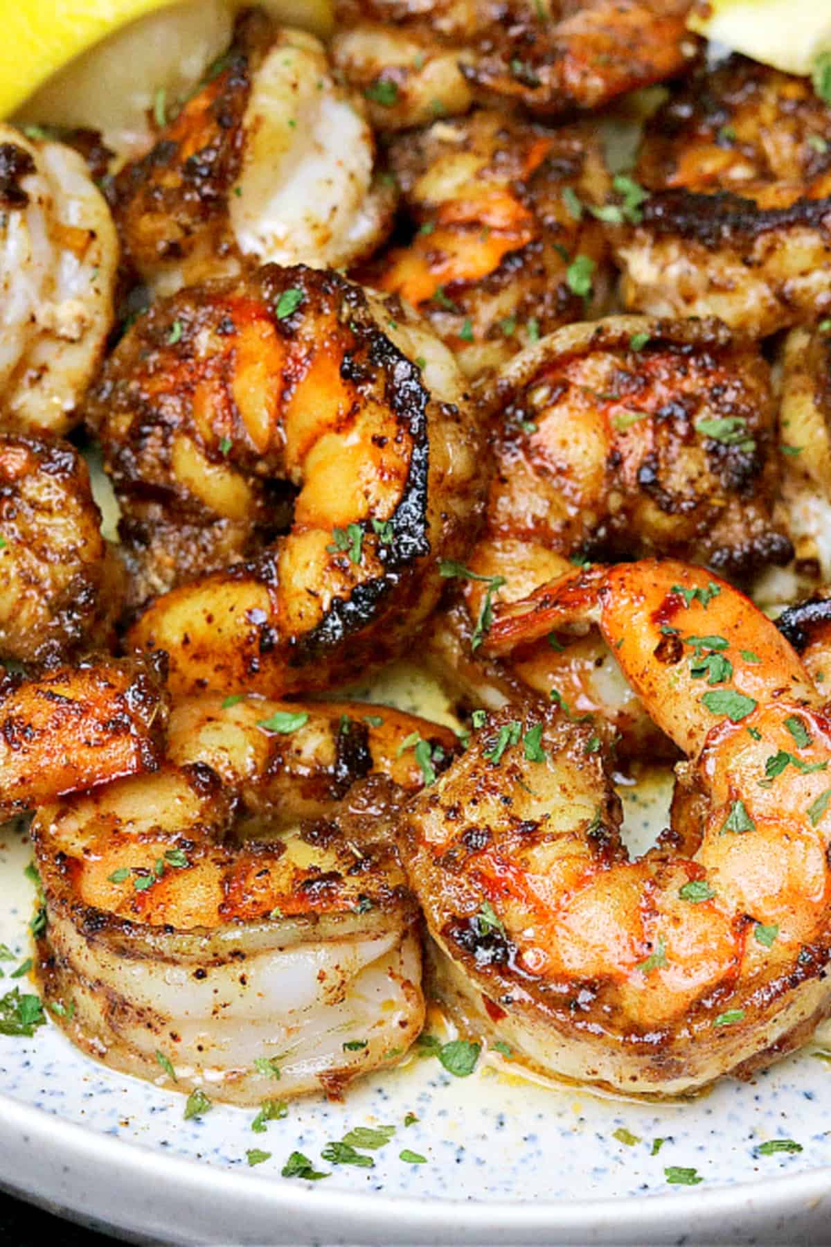 close-up photo of jumbo cast iron shrimp (pan seared shrimp) on a plate with lemon wedges. 