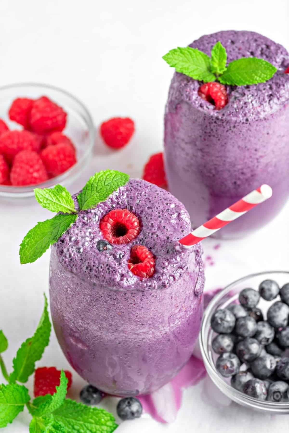 two keto berry smoothies in glass cups topped with fresh raspberries