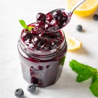 keto blueberry sauce in a glass jar with a spoon lifting sauce out.