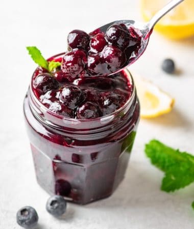 keto blueberry sauce in a glass jar with a spoon lifting sauce out.