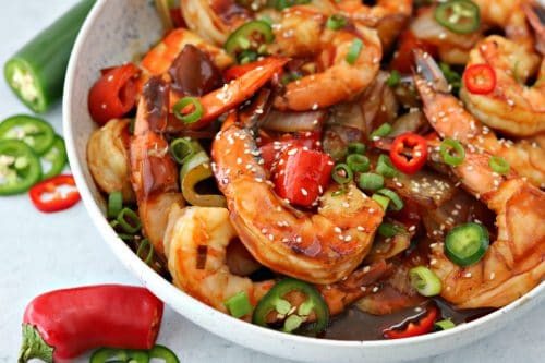 A bowl of food on a plate, with keto sweet and sour shrimp, sliced peppers, and sesame seeds
