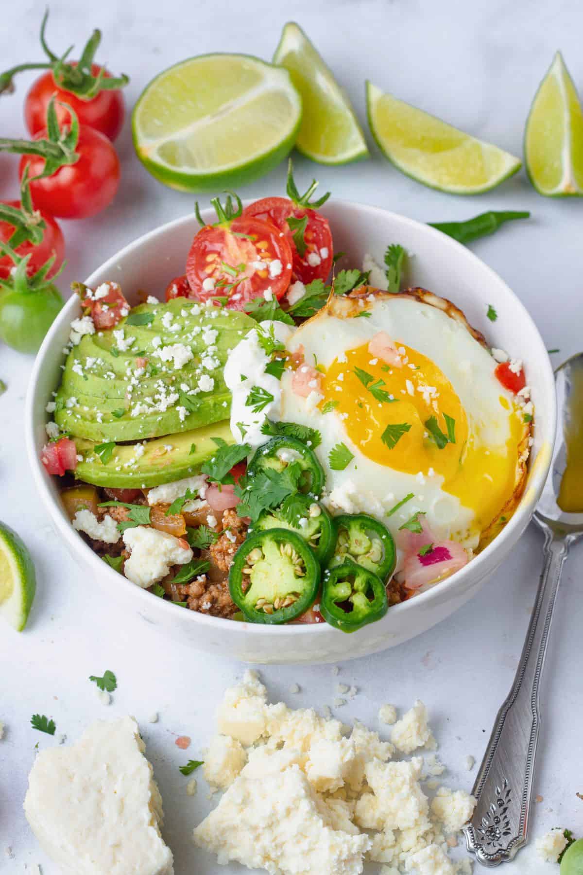 a breakfast taco bowl styled with lime, tomatoes, cotija cheese and eggs.