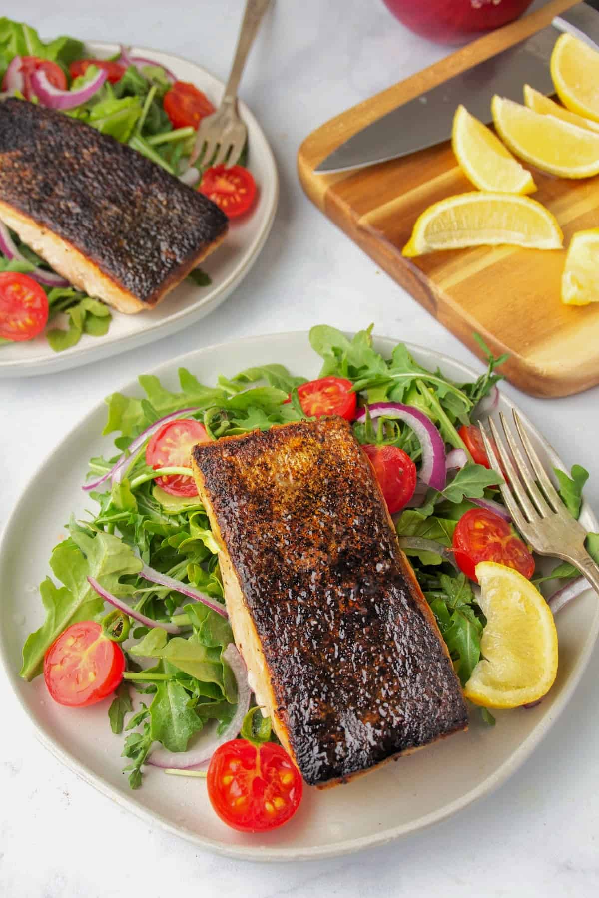 two simple green salads that include spring mix, cherry tomatoes, and red onions topped with cast iron crispy skin salmon