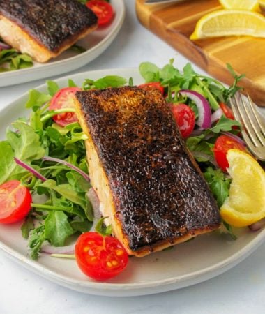 crispy skin salmon on a plate with a side salad and a wedge of lemon