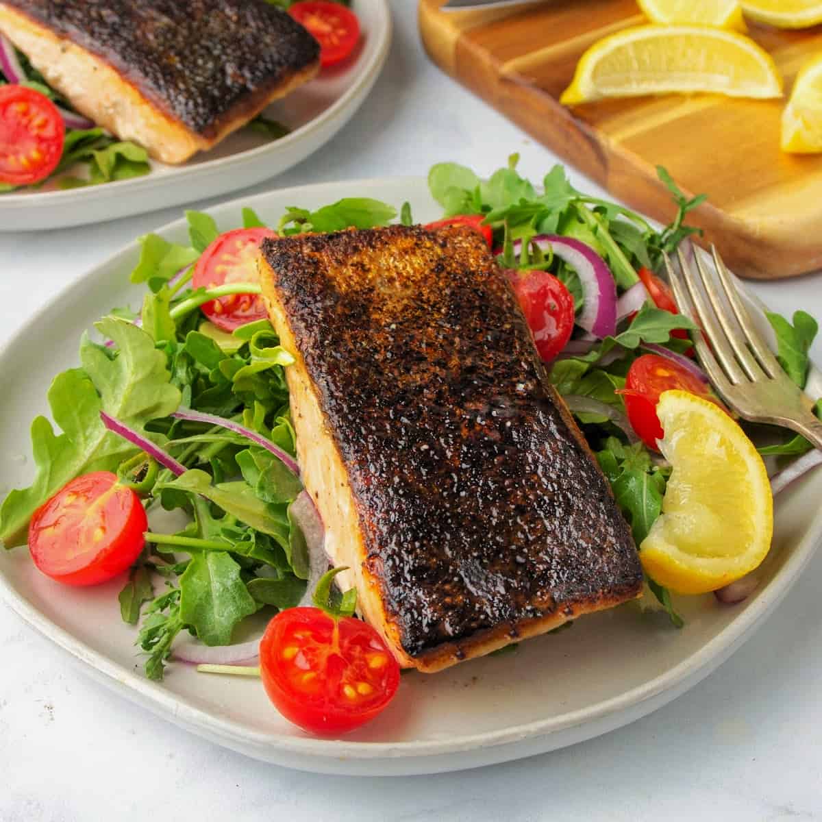 crispy skin salmon on a plate with a side salad and a wedge of lemon