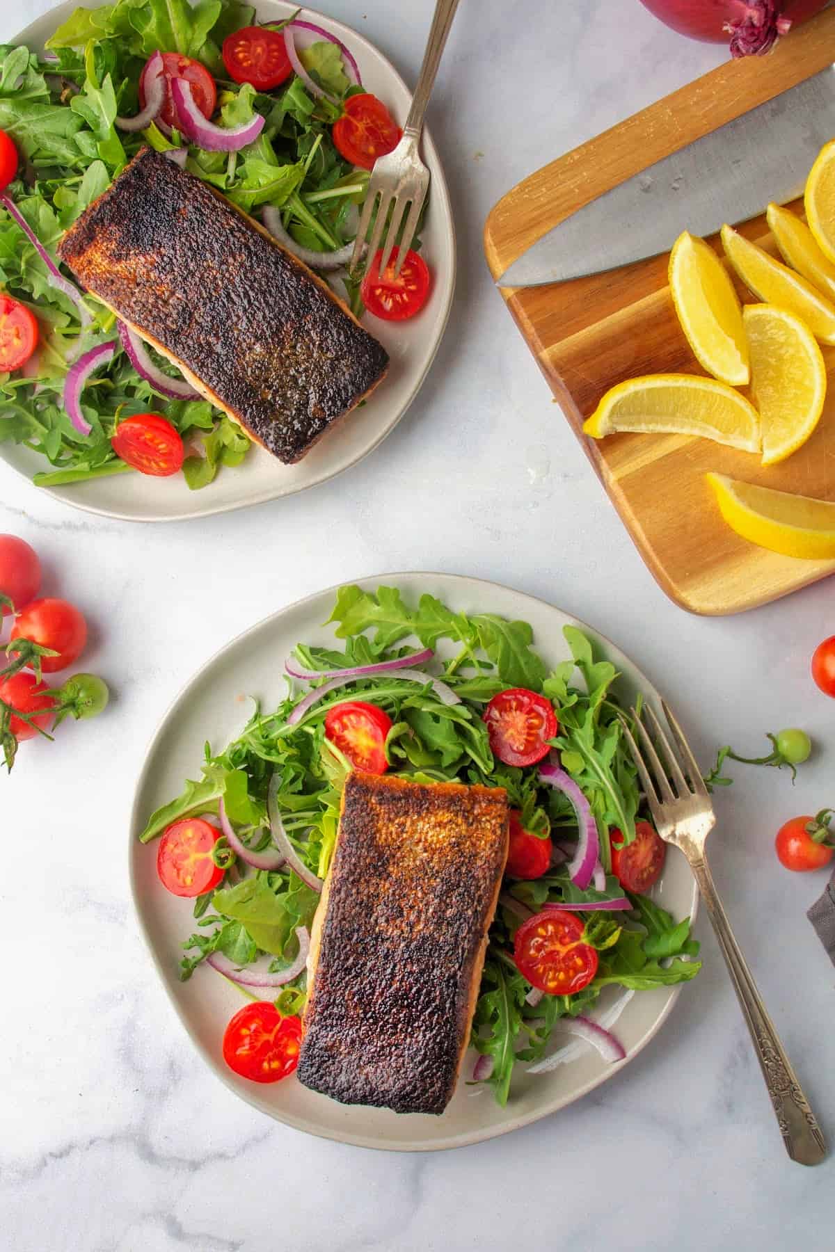 an overhead photo of pan seared salmon on two plates next to a cutting board with lemon wedges