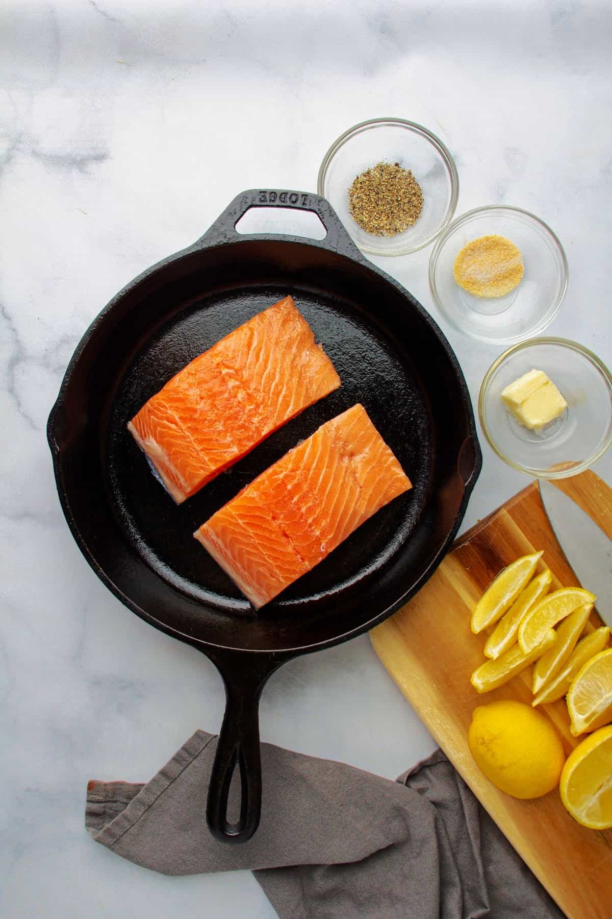 ingredients to make crispy skin salmon recipe in a separate bowls: two salmon filets, black pepper, garlic salt, butter, and lemon slices