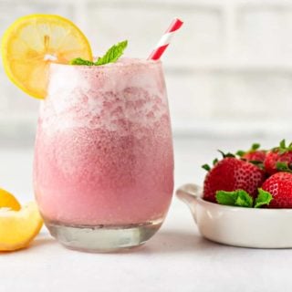 One glass of keto strawberry smoothie next to a small bowl of fresh strawberries