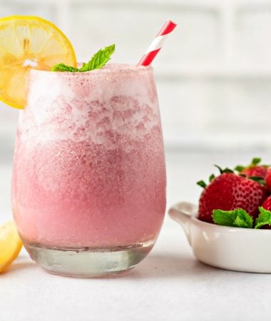 One glass of keto strawberry smoothie next to a small bowl of fresh strawberries