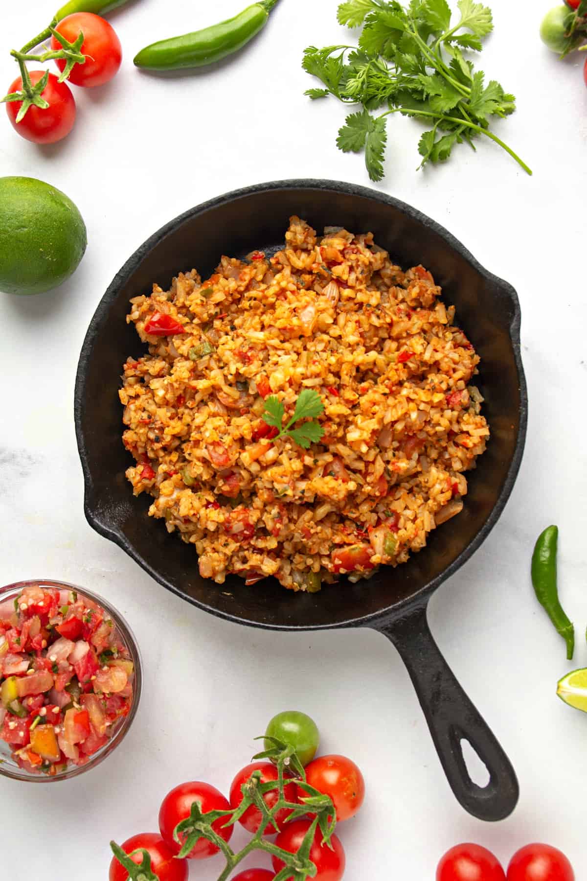 festive image of keto Spanish cauliflower rice with limes, jalapeños, and fresh cilantro