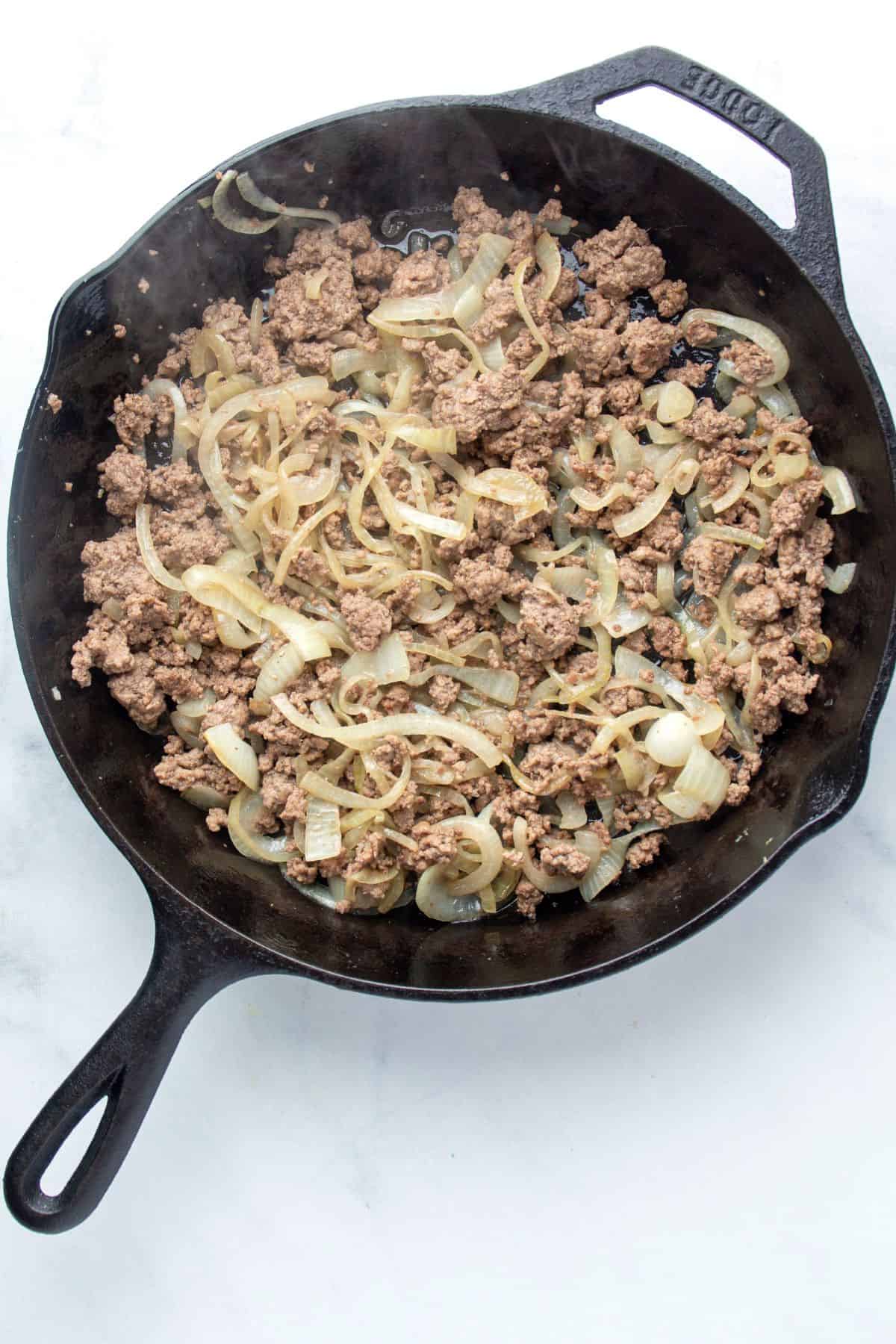 ground beef browned in a cast iron skillet with yellow onions