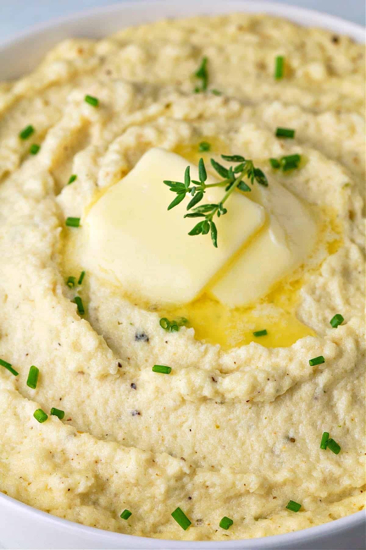 a close up of a bowl of mashed cauliflower with butter and herbs on top