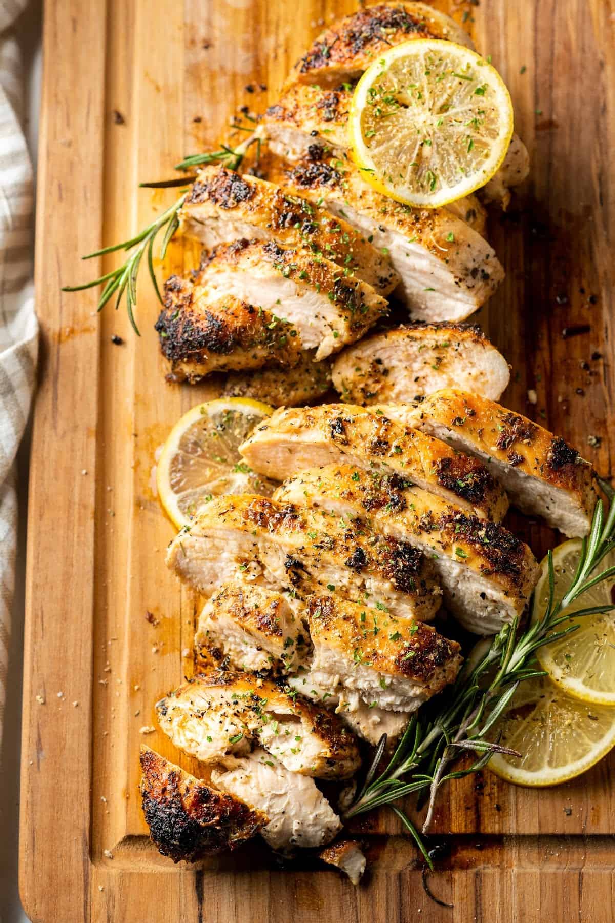 two sliced chicken breasts on a cutting board with lemon slices and rosemary