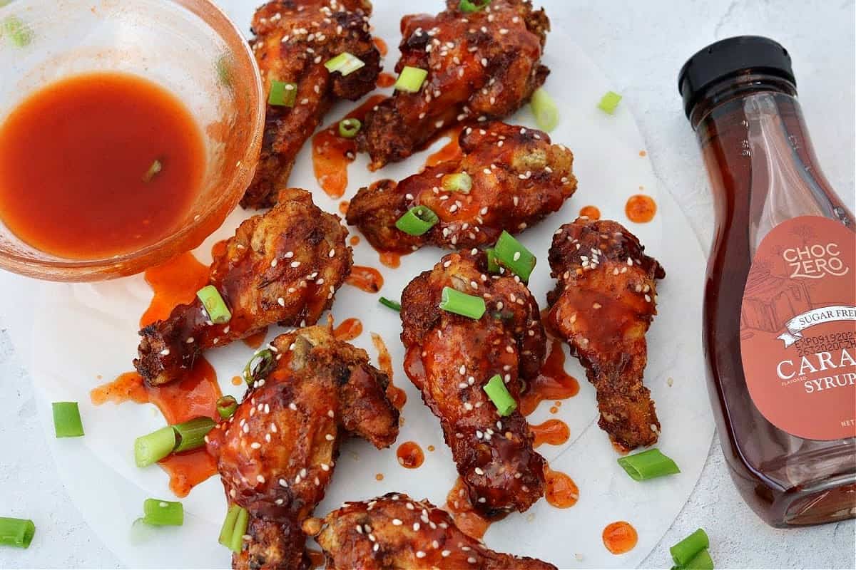 Keto Honey Sriracha Wings on parchment paper with a bottle of Choczero Caramel Syrup next to them. 