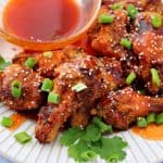 a close-up of honey sriracha chicken wings on a plate topped with green onions and sesame seeds