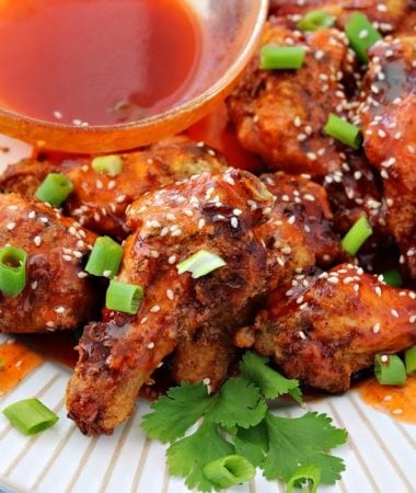 a close-up of honey sriracha chicken wings on a plate topped with green onions and sesame seeds