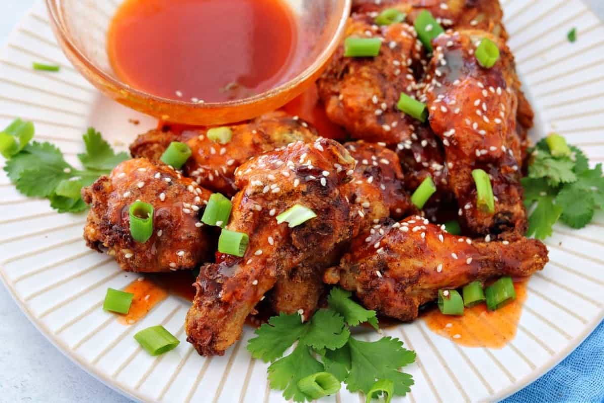 a close-up of honey sriracha chicken wings on a plate topped with green onions and sesame seeds