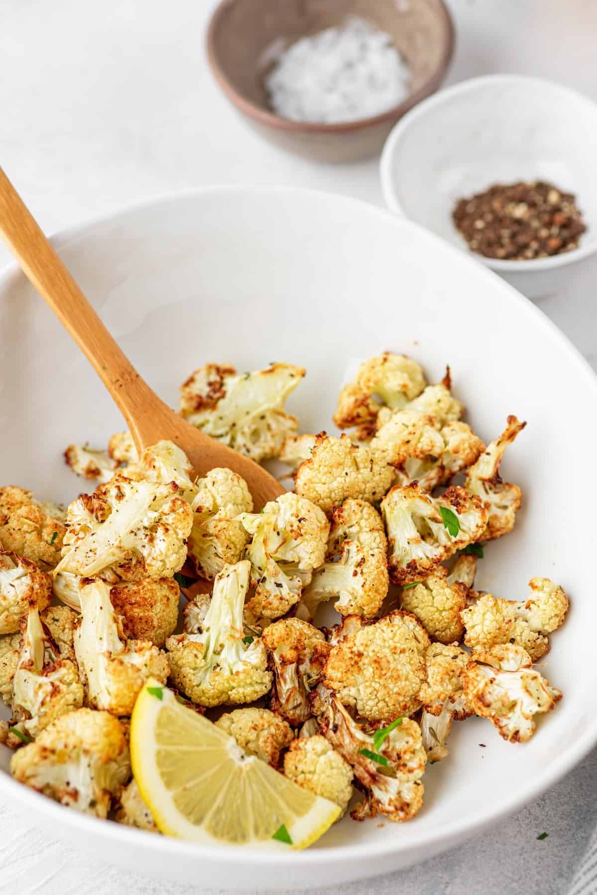 roasted cauliflower in a bowl with salt, pepper, and a lemon slice