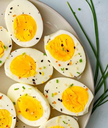 a close-up of hard boiled eggs on a plate topped with chives and everything bagel seasoning