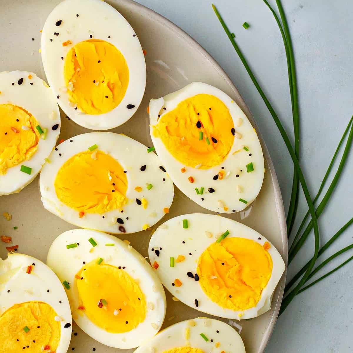 a close-up of hard boiled eggs on a plate topped with chives and everything bagel seasoning
