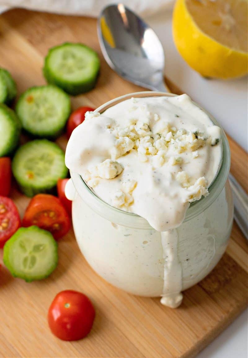 a glass jar filled with blue cheese dressing with sliced cucumbers and tomatoes