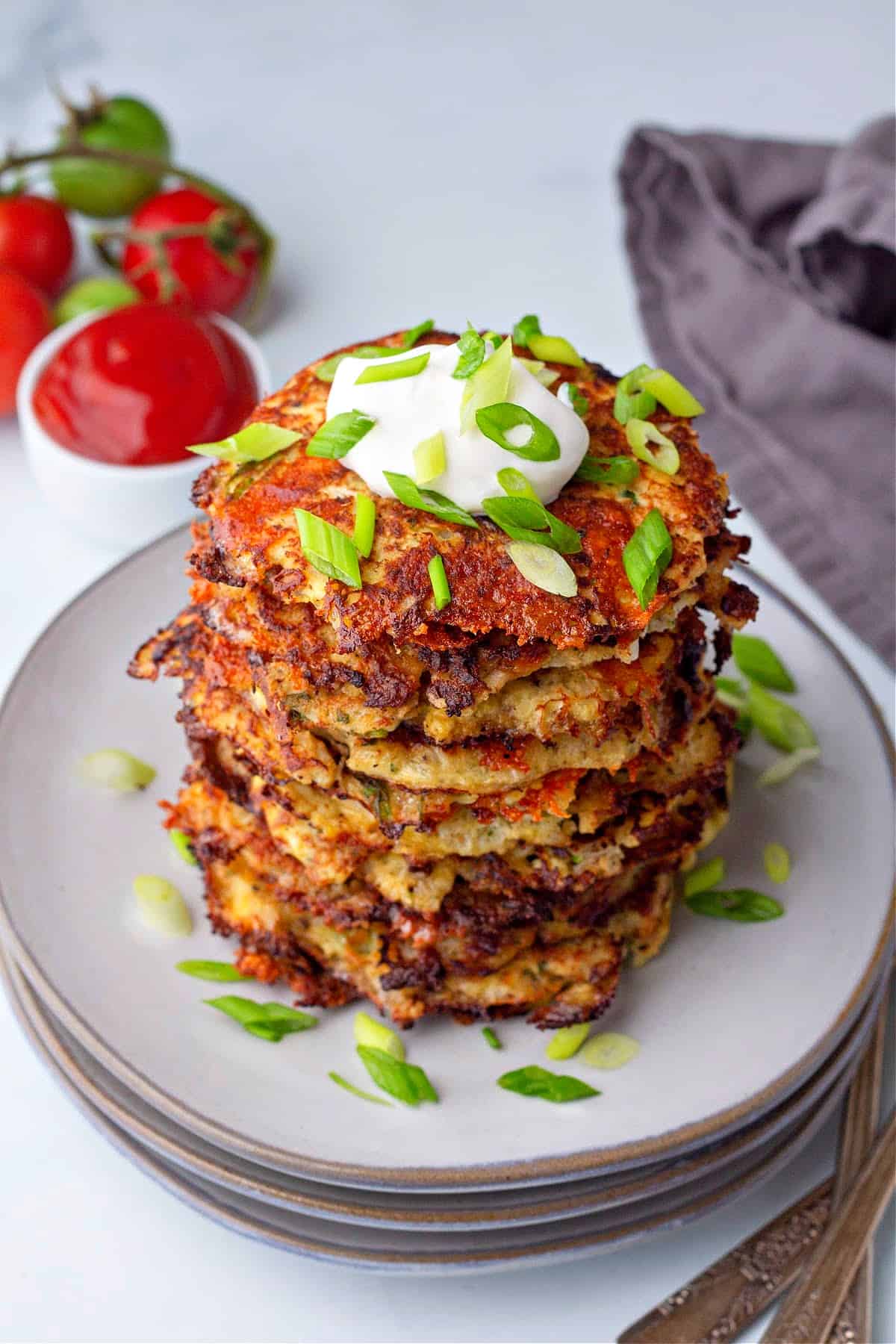 a vertical close up of a stack of cauliflower hash browns on a plate topped with sour cream and green onions