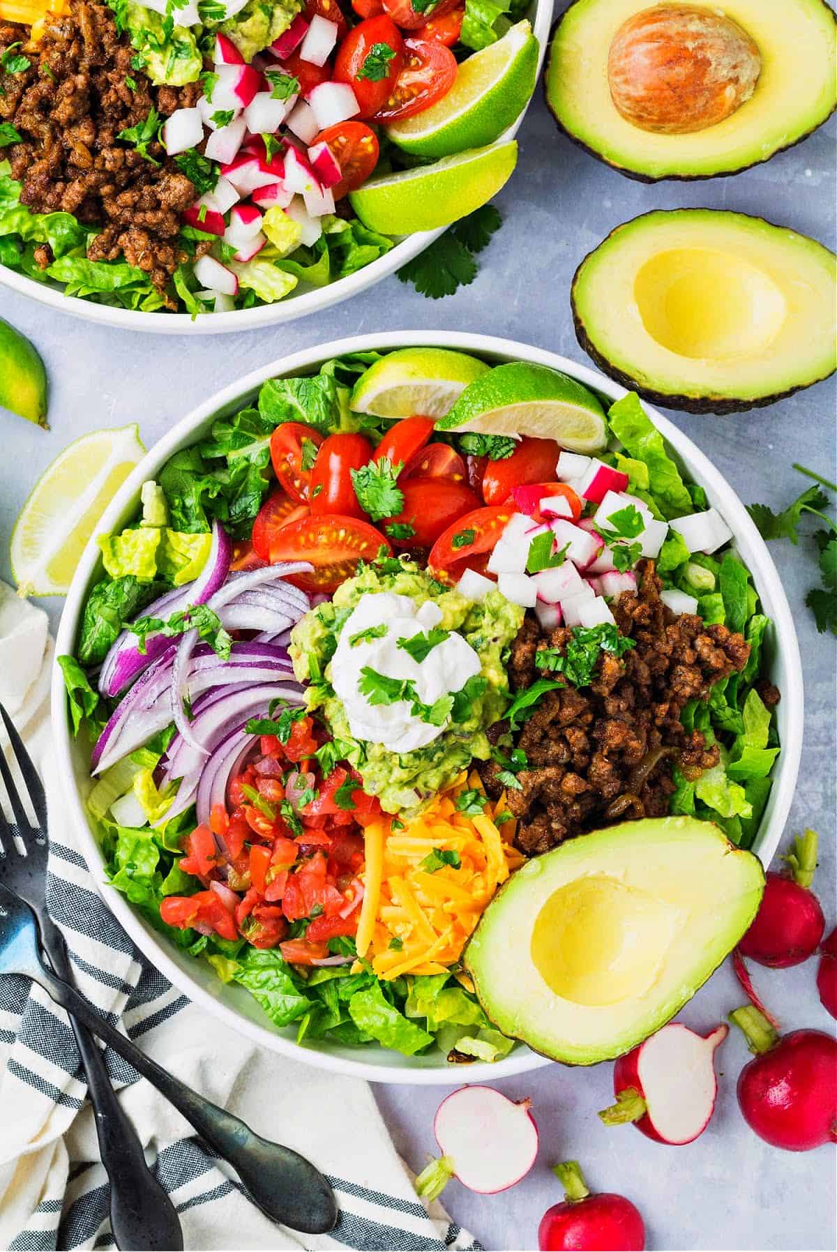 a bowl of keto taco salad with lettuce, tomatoes, taco meat, guacamole, radishes, cheddar, and Pico De Gallo