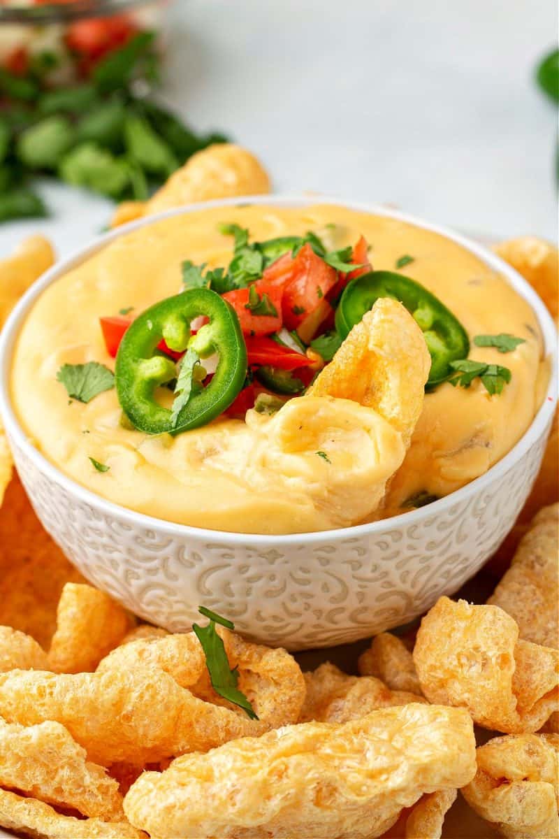 a close-up of homemade cheese dip in a bowl topped with tomatoes and jalapeños