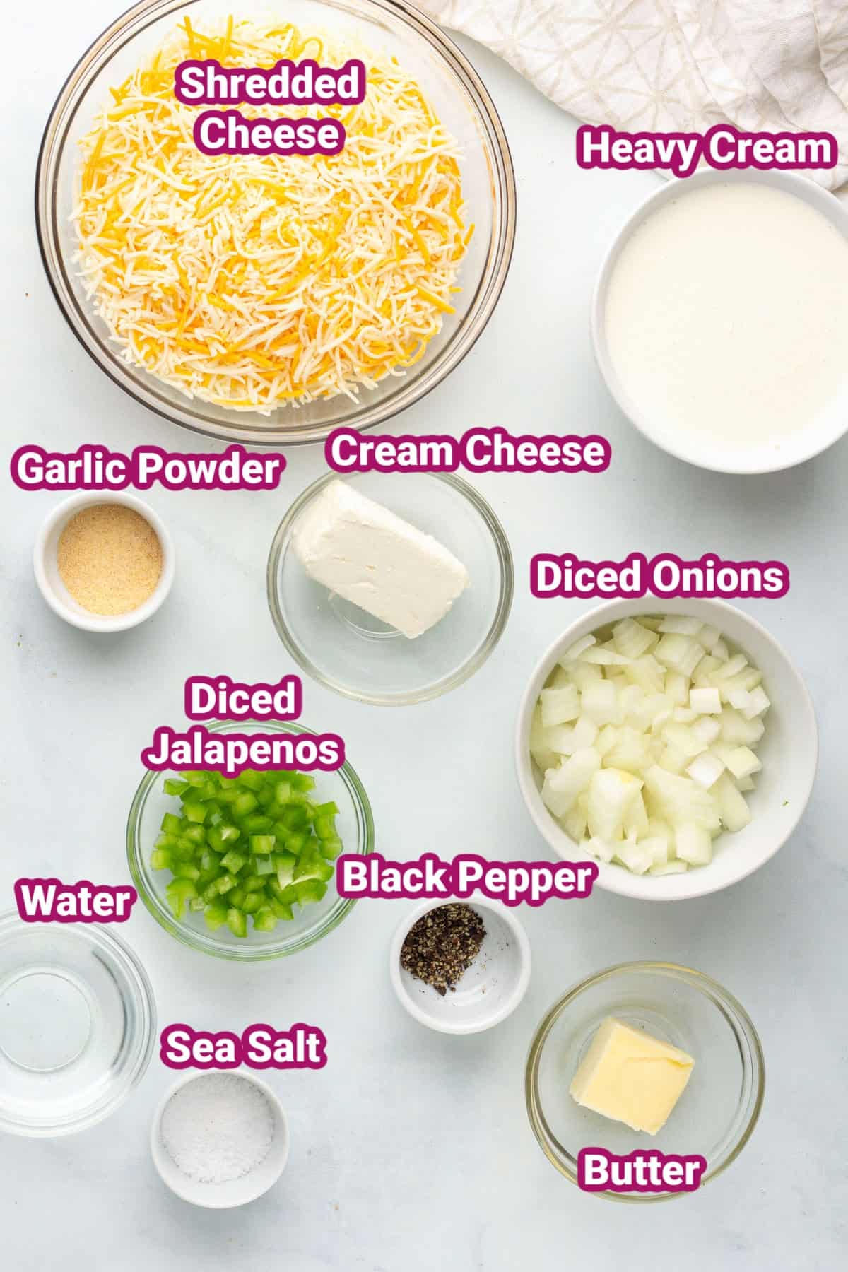 the ingredients in keto queso cheese dip recipe in separate bowls like shredded cheese, heavy cream, cream cheese, garlic powder, diced jalapeños, black pepper, diced yellow onion, water, sea salt and butter