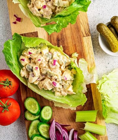 a close up of a tuna salad lettuce wrap on a cutting board with chopped vegetables