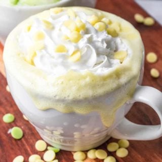 a close-up of keto white hot chocolate in a white mug with sugar-free white chocolate chips surrounding it