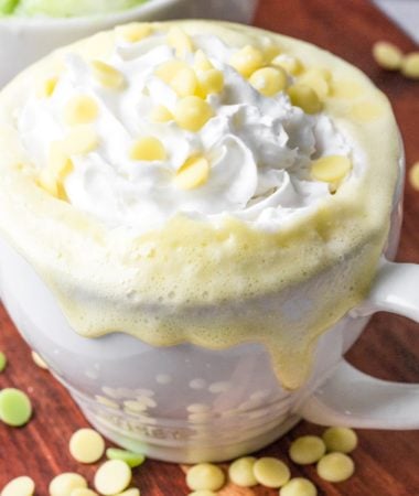 a close-up of keto white hot chocolate in a white mug with sugar-free white chocolate chips surrounding it