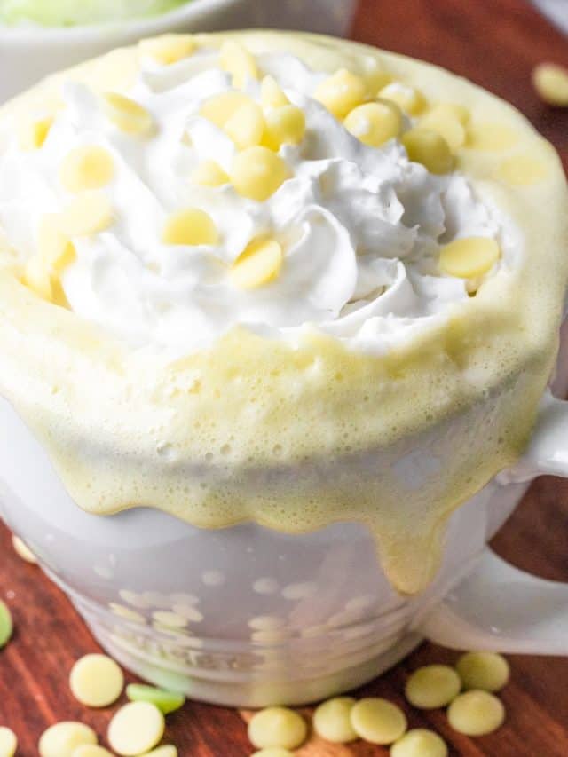 a close-up of keto white hot chocolate in a white mug with sugar-free white chocolate chips surrounding it