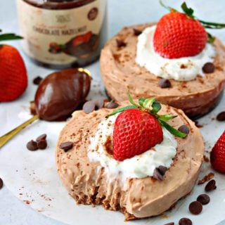 two keto chocolate cheesecakes on a parchment paper with keto Nutella chocolate hazelnut spread on a spoon