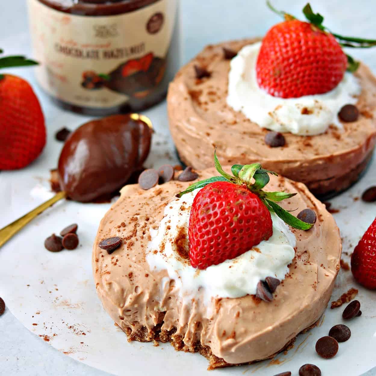 two keto chocolate cheesecakes on a parchment paper with keto Nutella chocolate hazelnut spread on a spoon