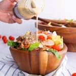 a close-up of Keto Cobb Salad in a brown bowl with dressing being poured on top
