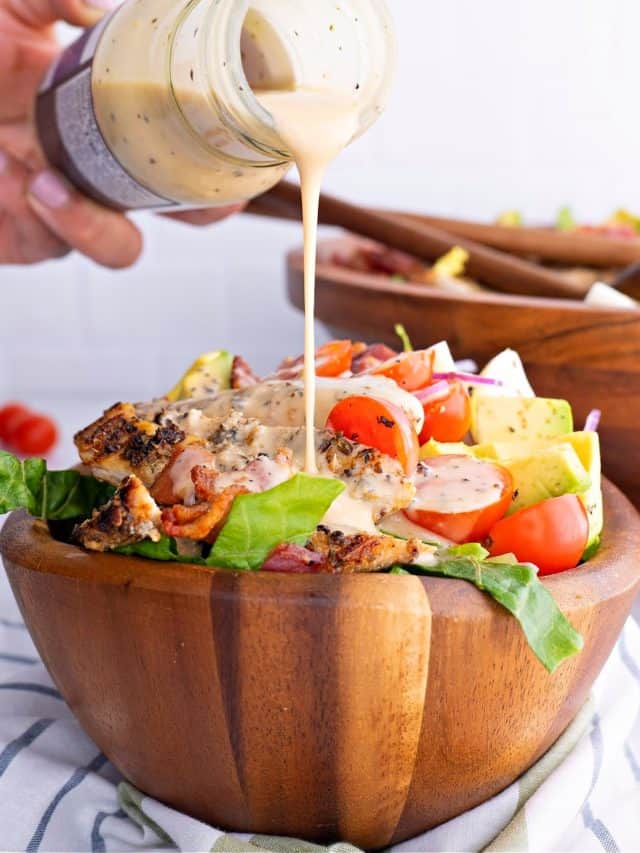 a close-up of Keto Cobb Salad in a brown bowl with dressing being poured on top