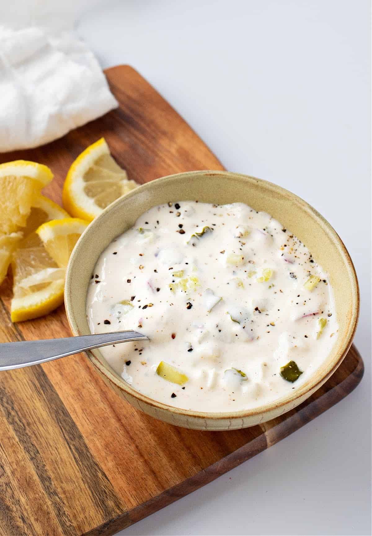 a bowl of homemade healthy tartar sauce in a bowl on a brown cutting board with lemon slices