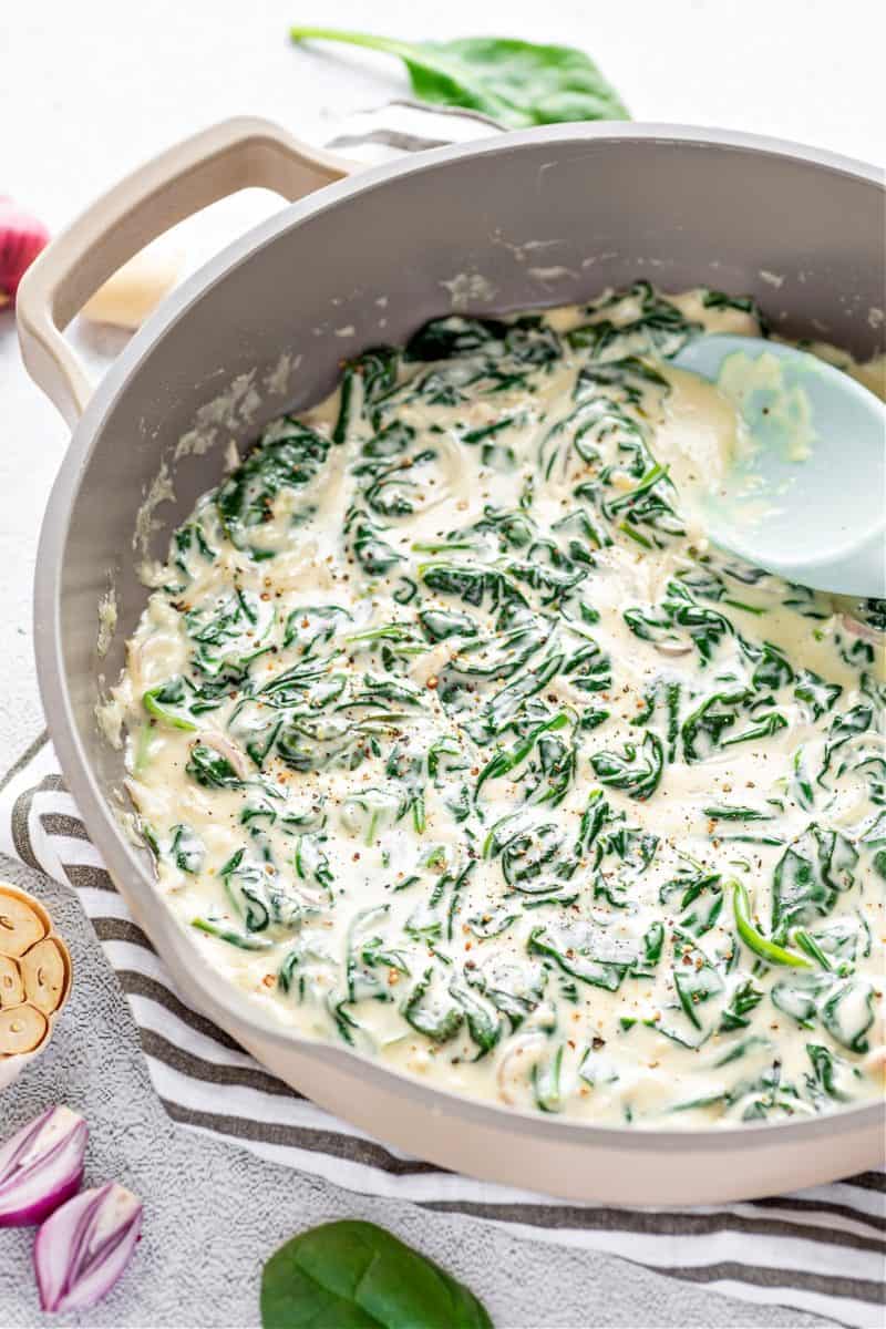 creamed spinach in a pot surrounded by garlic cloves, spinach leaves, and shallots